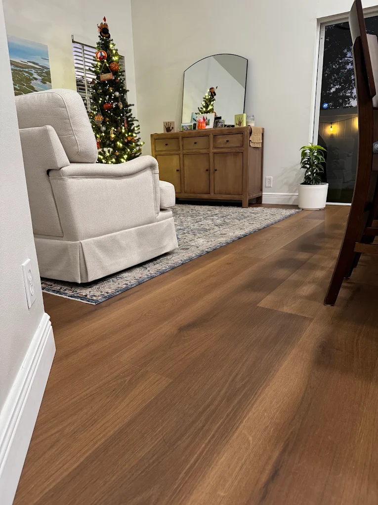 Warm brown wide-plank flooring installed by Ozzifloors in a living room with an armchair and a Christmas tree